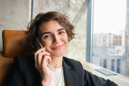 Close up portrait of corporate woman laughing and smiling, talking over the phone, sitting in office.