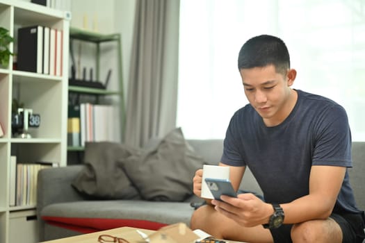 Smiling man drinking coffee and checking social media or chatting with friends on mobile phone.