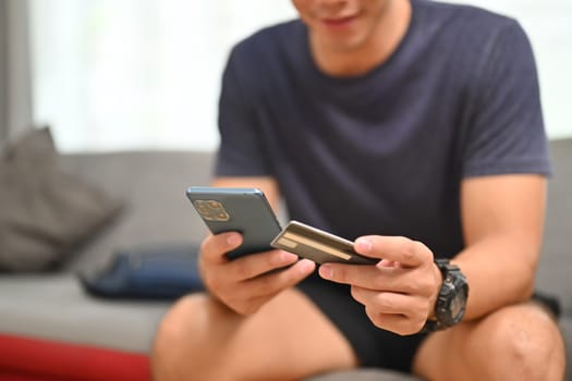 Cropped shot of casual man holding credit card and using mobile phone for shopping online.