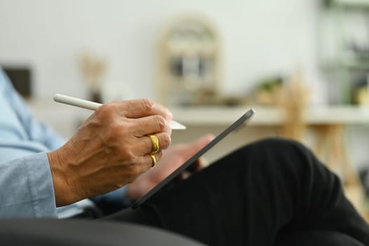 Side view of mature man sitting on sofa and using digital tablet. Retirement lifestyle and technology concept.