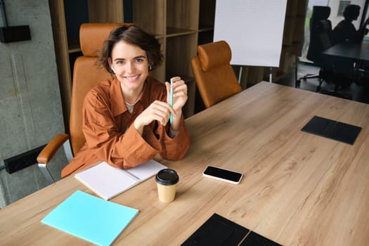 Portrait of young female entrepreneur, employee working in office, writing down, making notes in conference room, smiling.
