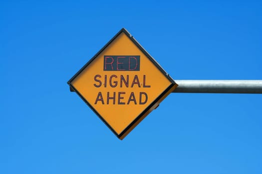 A Red signal ahead sign against blue sky