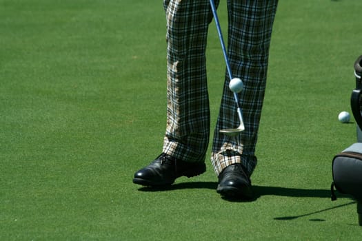 A Golfer juggling a golf ball with retro pants
