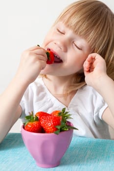 Little girl eating delicious ripe strawberries, bowl in front of her.