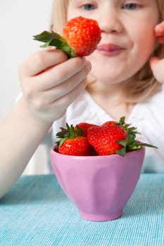 Little girl eating delicious ripe strawberries, bowl in front of her.