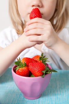 Little girl eating delicious ripe strawberries, bowl in front of her.
