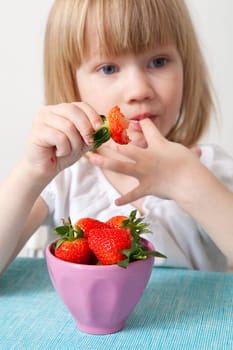 Little girl eating delicious ripe strawberries, bowl in front of her.