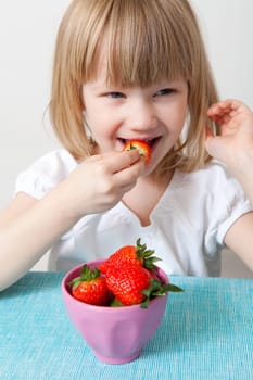 Little girl eating delicious ripe strawberries, bowl in front of her.