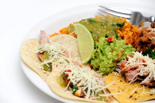Mexican style meal of Pork Carnitas soft tacos with refried beans, Spanish rice topped with fresh salsa verde and spicy guacamole.