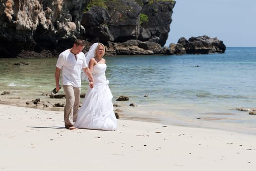 Honeymoon on the beach,bride with wedding dress and husband walking by the sea