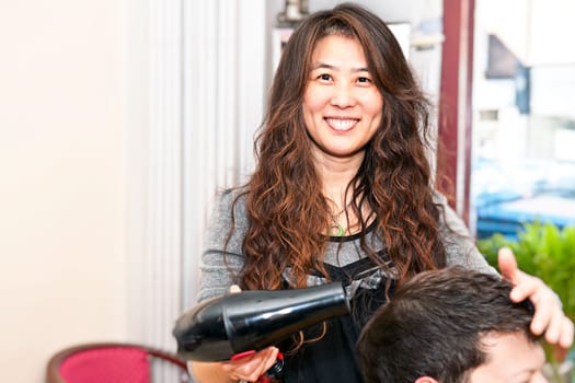 Smiling hairstylist drying hair with hairdryer in her salon