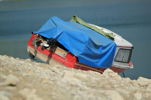 Small red and blue boat ran aground on the rocks of Gruyere lake, Fribourg, Switzerland, because of dryness