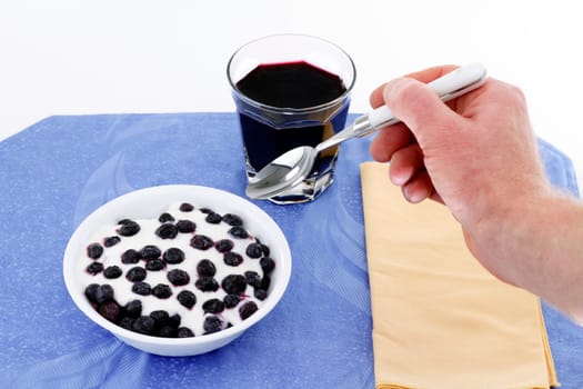 Man&#039 s hand with spoon ready to eat bowl of yogurt with blueberries, and drink blueberry juice.