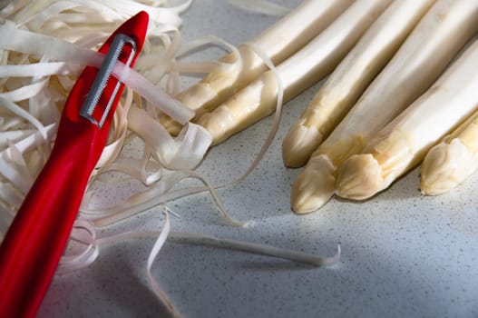 Wite asparagus with red peeler in kitchen