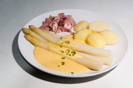 Meal with white asparagus and potatoes in sauce hollandaise.