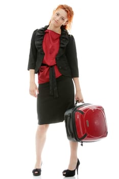 Young redhead businesswoman (deaf with hearing aid) with red suitcase, isolated on white background