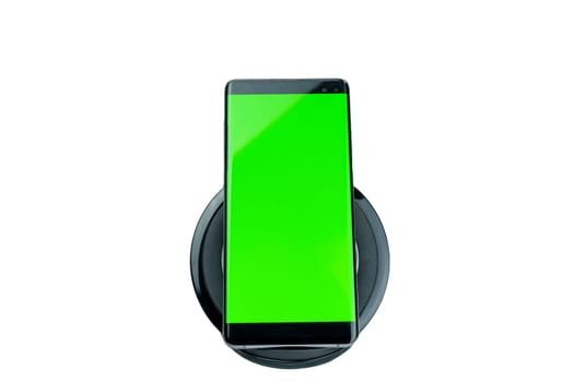 Modern smartphone with a bright green screen placed on a wireless charging pad, isolated on a white background, suitable for mockups and design presentations.