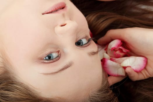 Close-up of beautiful young woman face with long blond hair and rose-petal