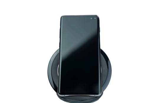 Close-up of a modern black smartphone placed on a wireless charging pad, isolated on a white background, showing technology and convenience.