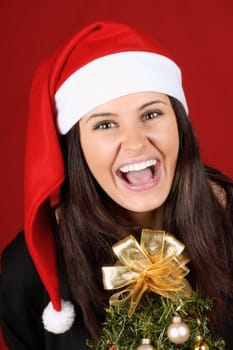Beautiful 18 years old Santa Claus girl laughing in front of Christmas tree over a red background