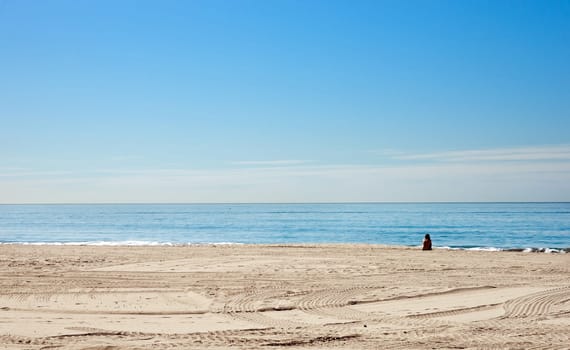 a single woman sits alone on the beach in california
