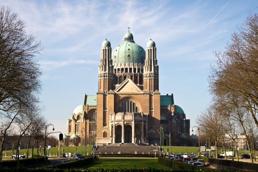 The Basilica of the Sacred Heart in Brussels ranks fifth among the largest churches in the world. The large Art Deco building is catched in the sunlight against a light-blue sky with some clouds.