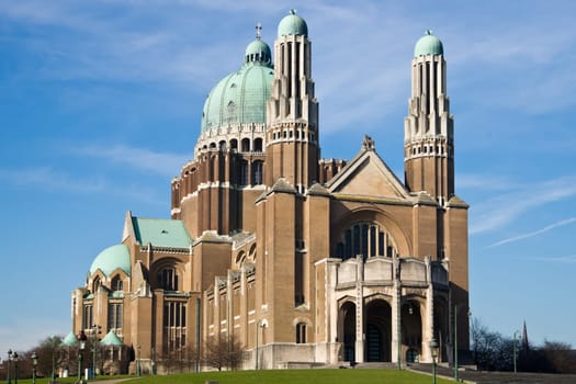 The Basilica of the Sacred Heart in Brussels ranks fifth among the largest churches in the world. The large Art Deco building is catched in the sunlight against a light-blue sky with some clouds.