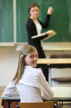 Schoolchild with teacher in classroom. The schoolgirl turns around and smiles