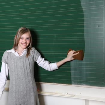 Schoolgirl at the blackboard. She wipes the blackboard and smiles - Textfreiraum