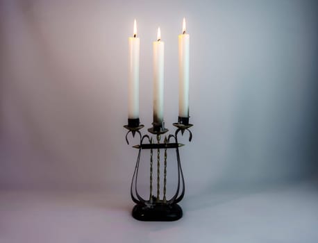 Elegant antique candelabrum with three lit candles, casting a soft warm glow on a neutral gray background. Perfect for vintage, romantic, and classic interior themes