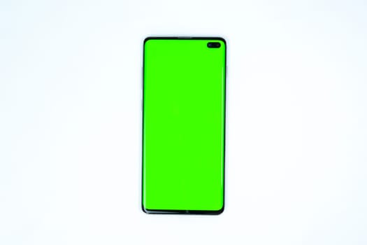 Modern smartphone with a bright green screen placed on a wireless charging pad, isolated on a white background, suitable for mockups and design presentations.