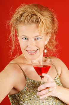 Portrait of a beautiful blond woman with blue eyes, wearing a green sequins top, holding a red drink, over a red background.