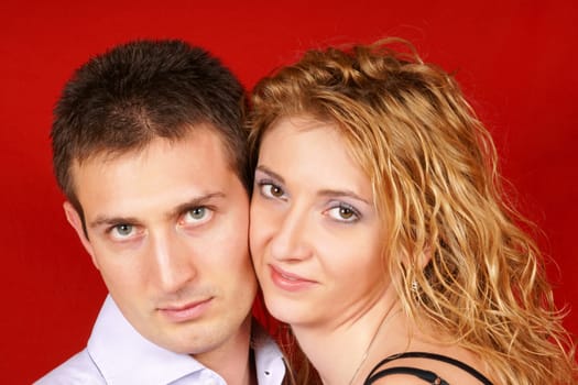 Beautiful young couple in love looking at camera over a red background. Soft focus.