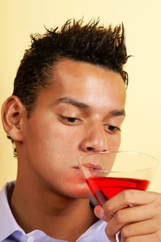 Sad young man drinking red cocktail from a martini glass.