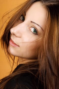 Portrait of a young woman with green eyes and brown hair over a yellow background