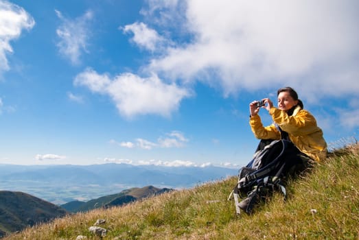 Young person relaxes on hiking in mountains and taking photo with mobile phone