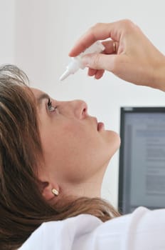 Detail of young business woman applying eye drops on workplace - computer monitor in background
