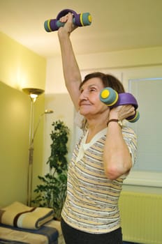 Active senior woman exercising at home with barbells