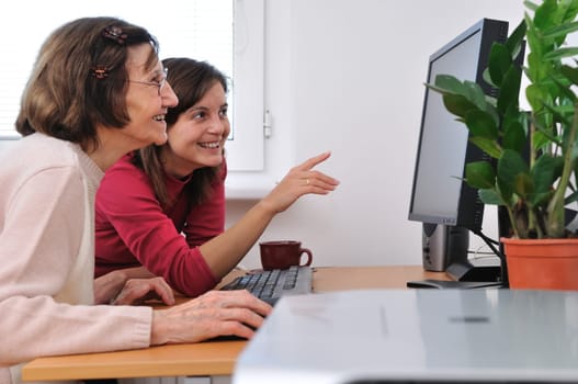 Young woman teaches her grandmother work with computer - senior lifestyle