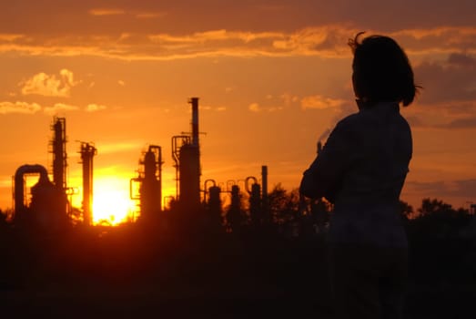 Woman looks on oil refinery at sunset (silhouette)