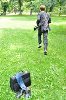 Escape from civilization concept - business man running in park away from bag, shoes and tie