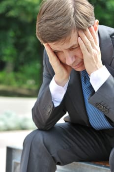 Portrait of depressed senior business man with head in hands siting on bench outdoors