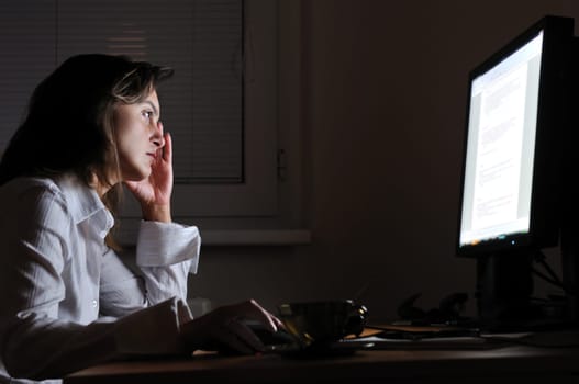 Neck pain - young tired business woman working overtime at computer, night setting
