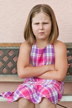 Outdoors portrait of small cute girl sitting on bench with offended expression