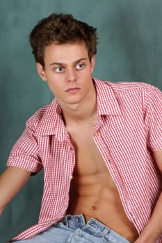 Portrait of a young man with unbuttoned chequered shirt over a green background