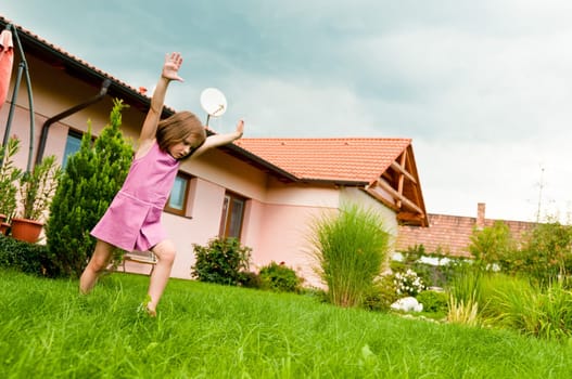 Small girl making cartwheel on garden with family house in background