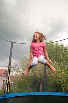 Small cute child jumping on trampoline - garden and family house in background