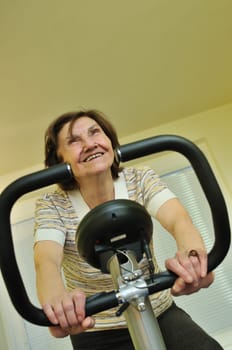 80 something mature woman exercises on spinning bicycle at home