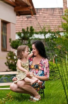Mother with daughter siting on bench in garden - family house in background