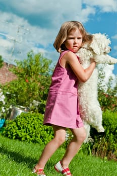 Small cute girl carrying her dog in garden behind family house